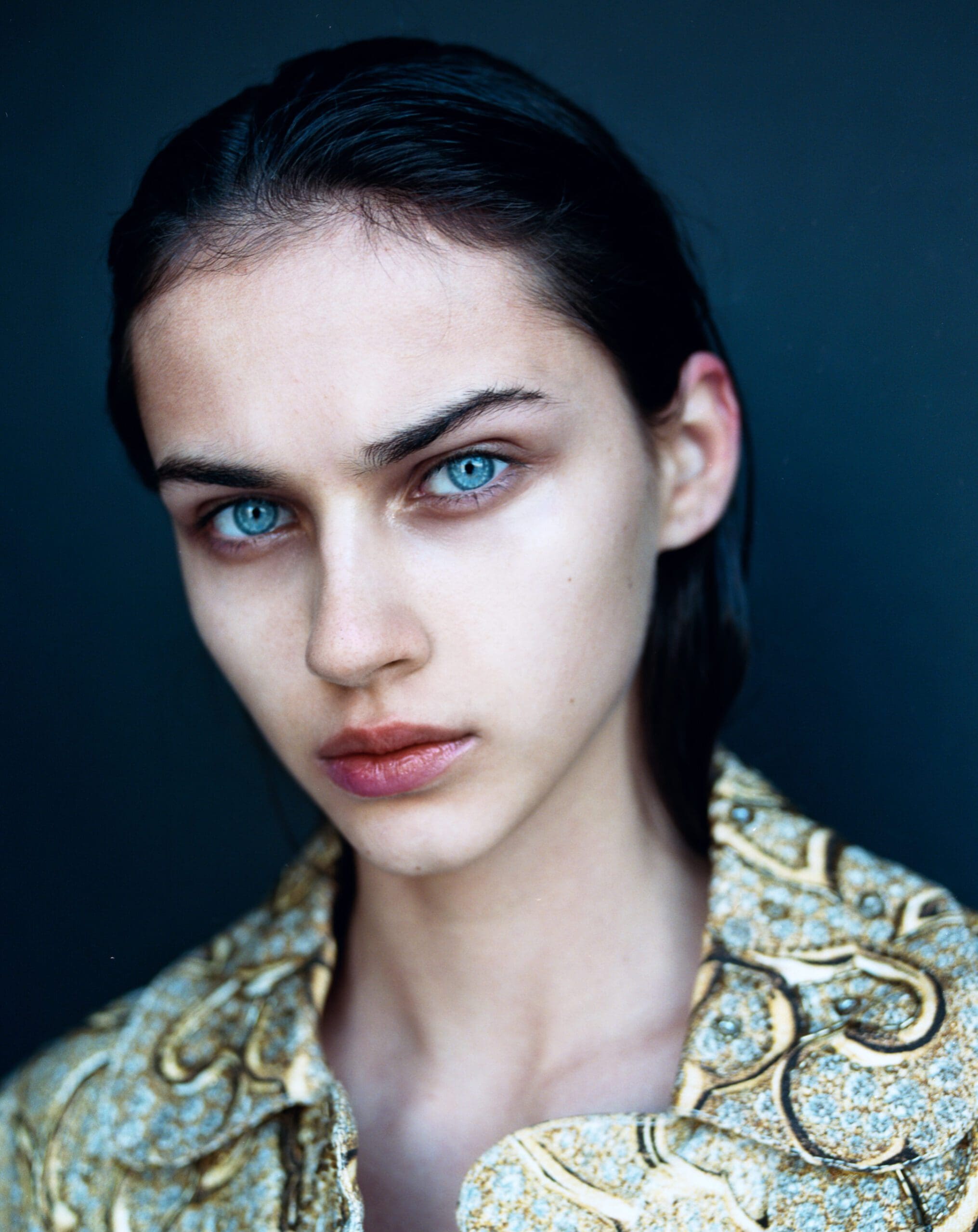 Portrait of a woman with blue eyes in a gold patterned jacket