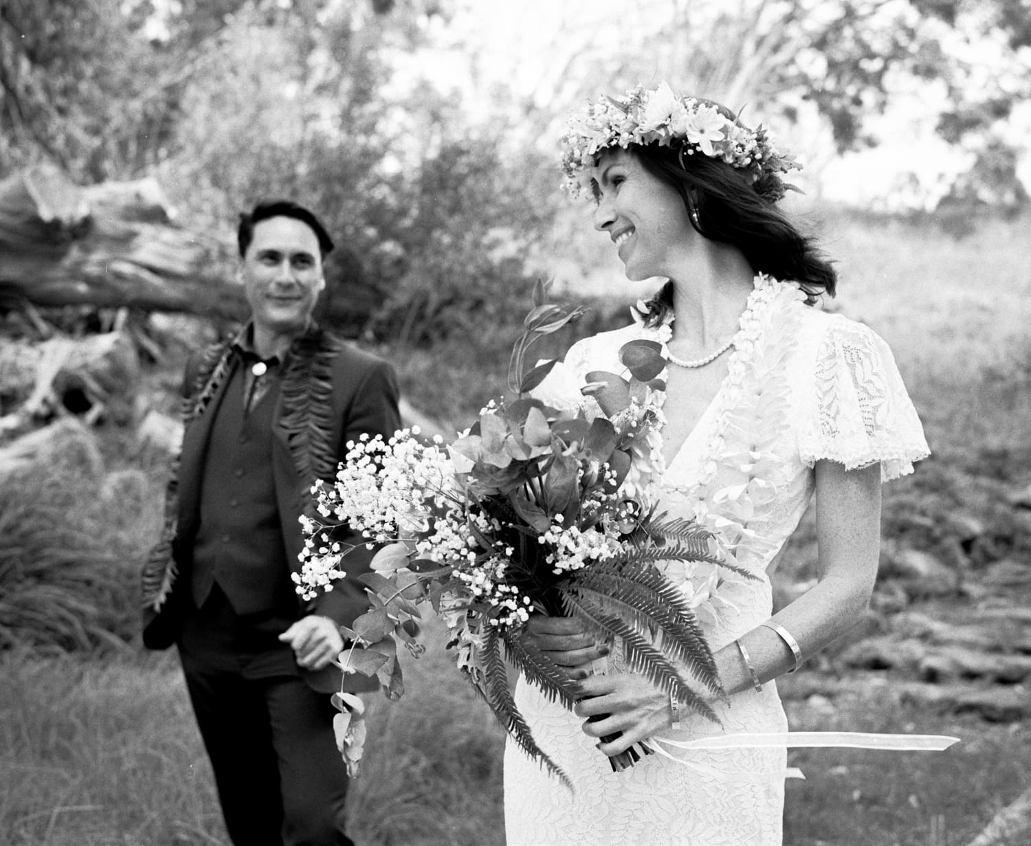 Black and white portrait of a bride with a flower crown and bouquet beside her groom