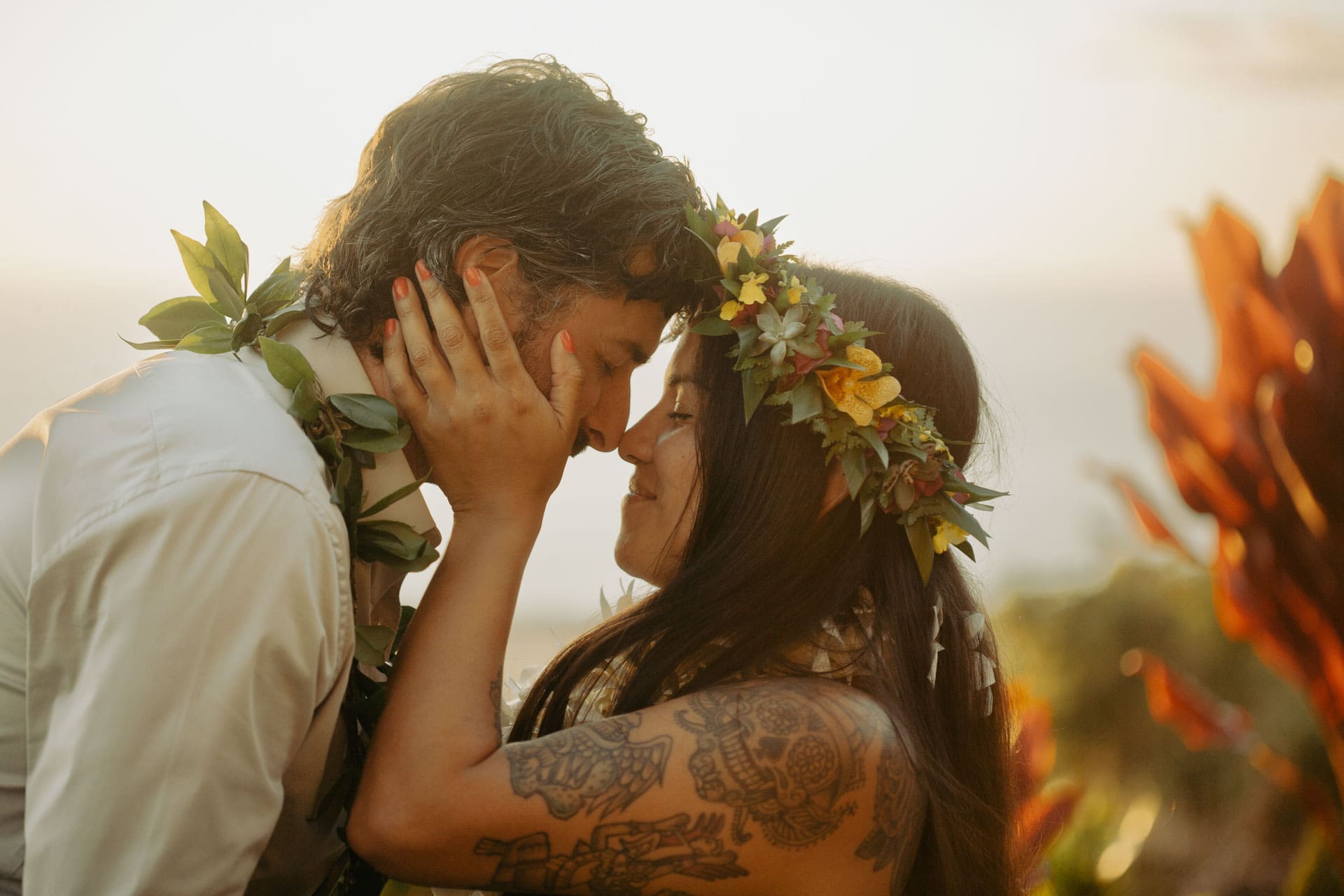 Bride and groom touching foreheads at sunset in flower crowns and leis