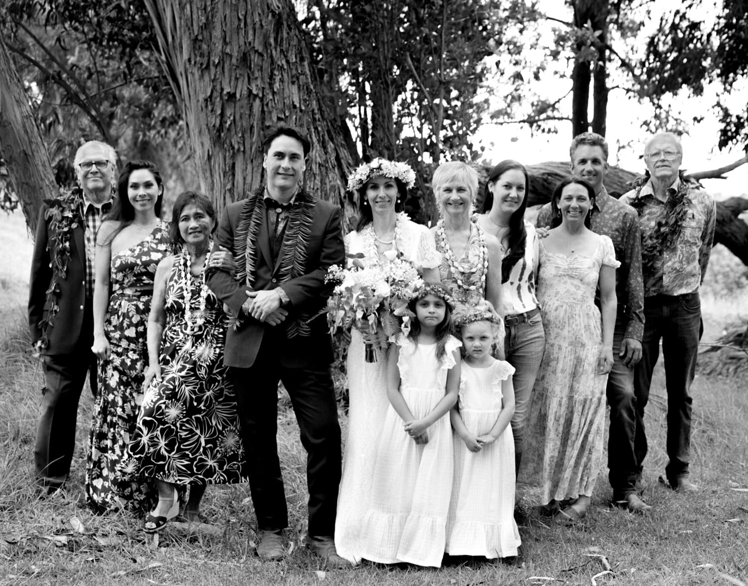 Black and white group photo of a wedding party and family under a large tree