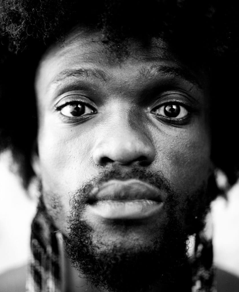 Close-up black and white portrait of a man with an afro looking into the camera