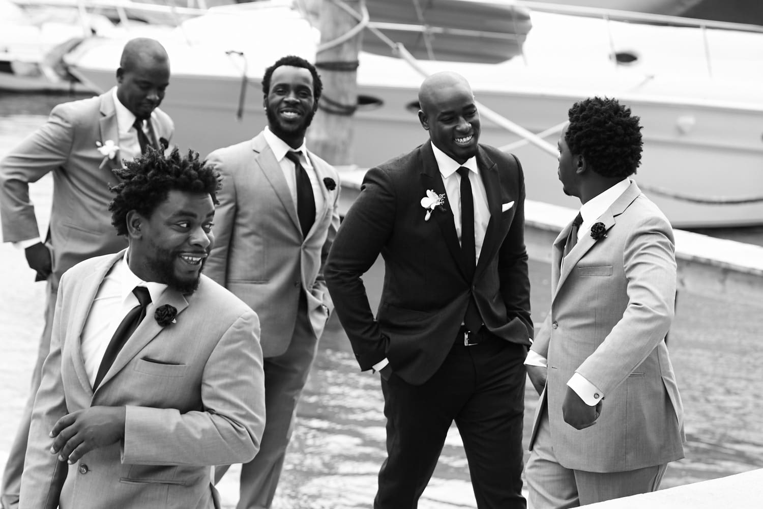 Black and white candid of groomsmen laughing beside a yacht, wedding in Miami