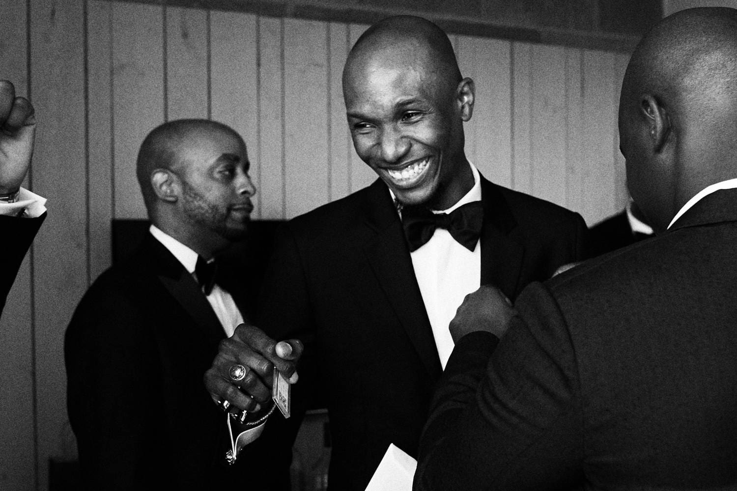 Black and white candid of groomsmen laughing and adjusting a bow tie, wedding in New York City