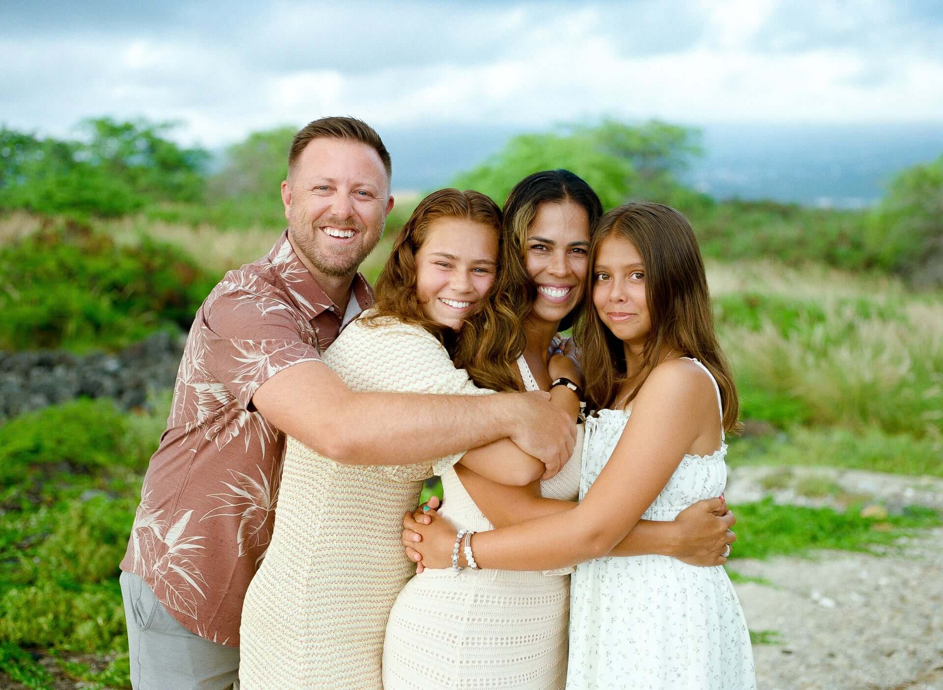 Family of four in a close hug on a grassy hillside