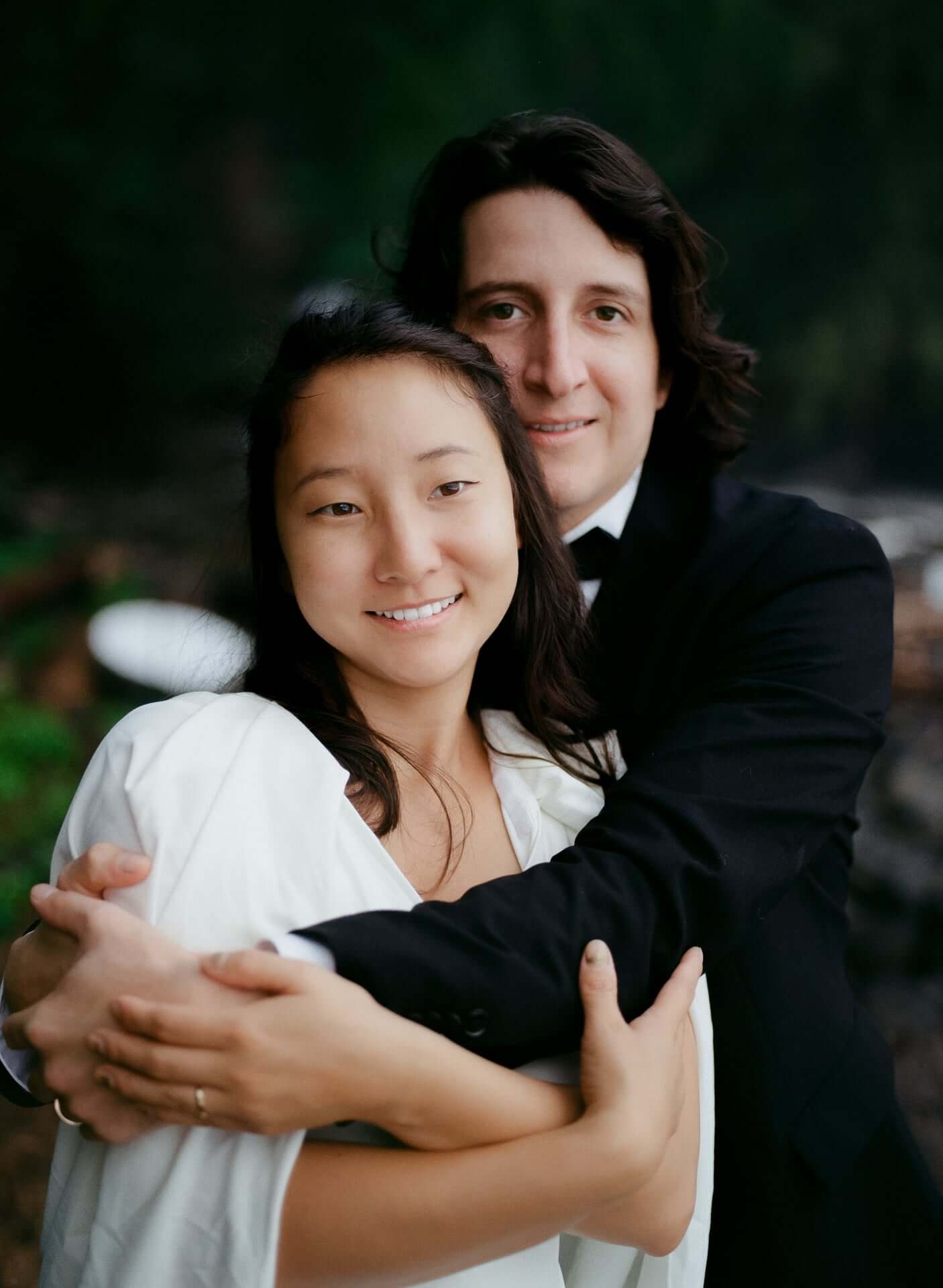 Bride and groom embracing outdoors among green foliage