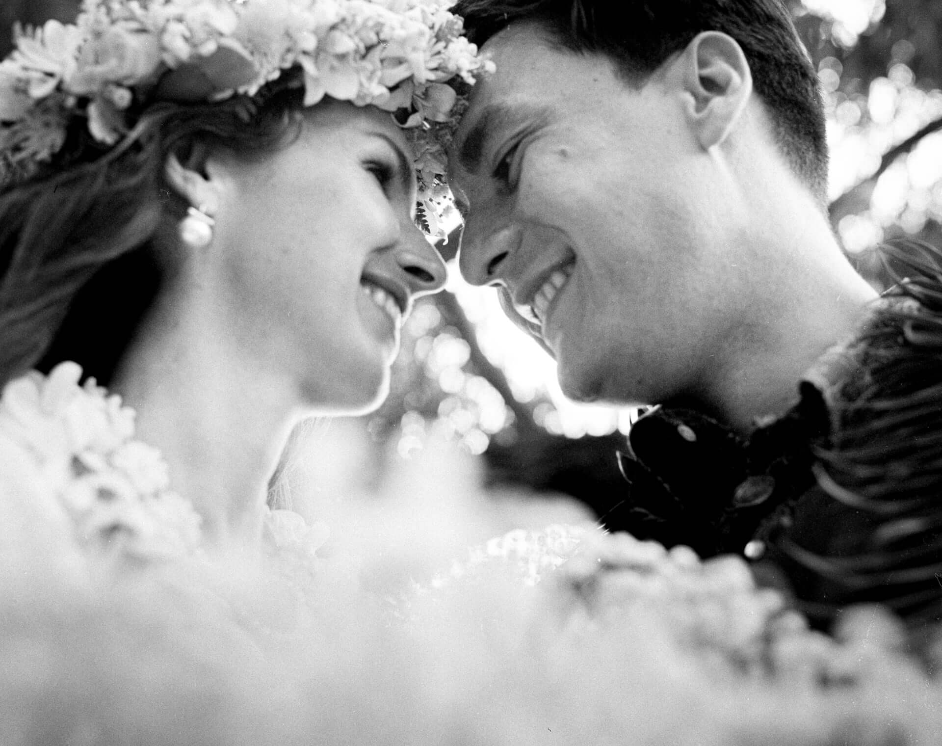 Black and white close-up of a smiling couple touching foreheads, the bride in a flower crown