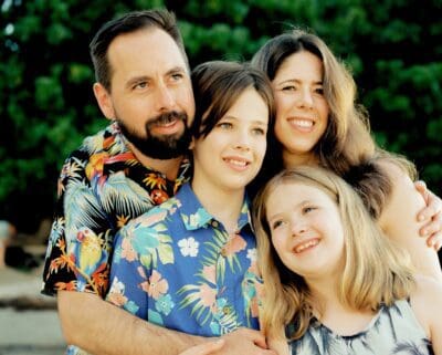 Family portrait on Kona beach at sunset by a photographer in Hawaii, featuring soft golden hour light and a beach backdrop.