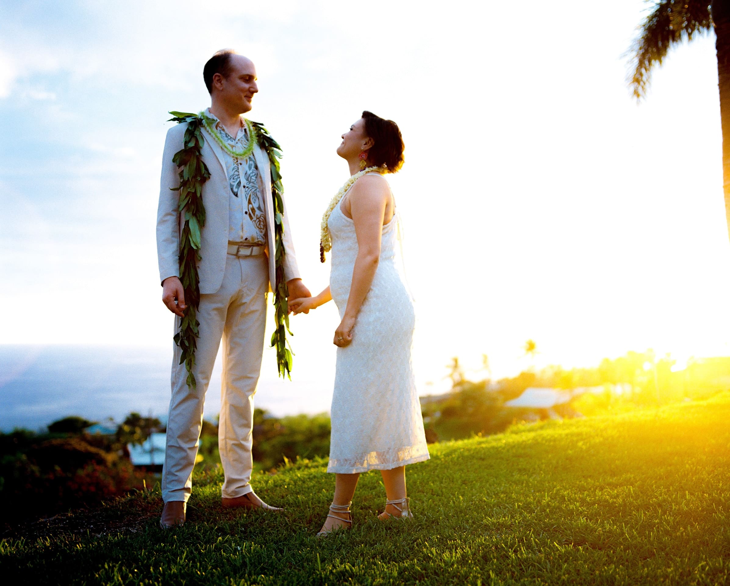 Bride and groom holding hands on a lawn at golden hour with the ocean behind them