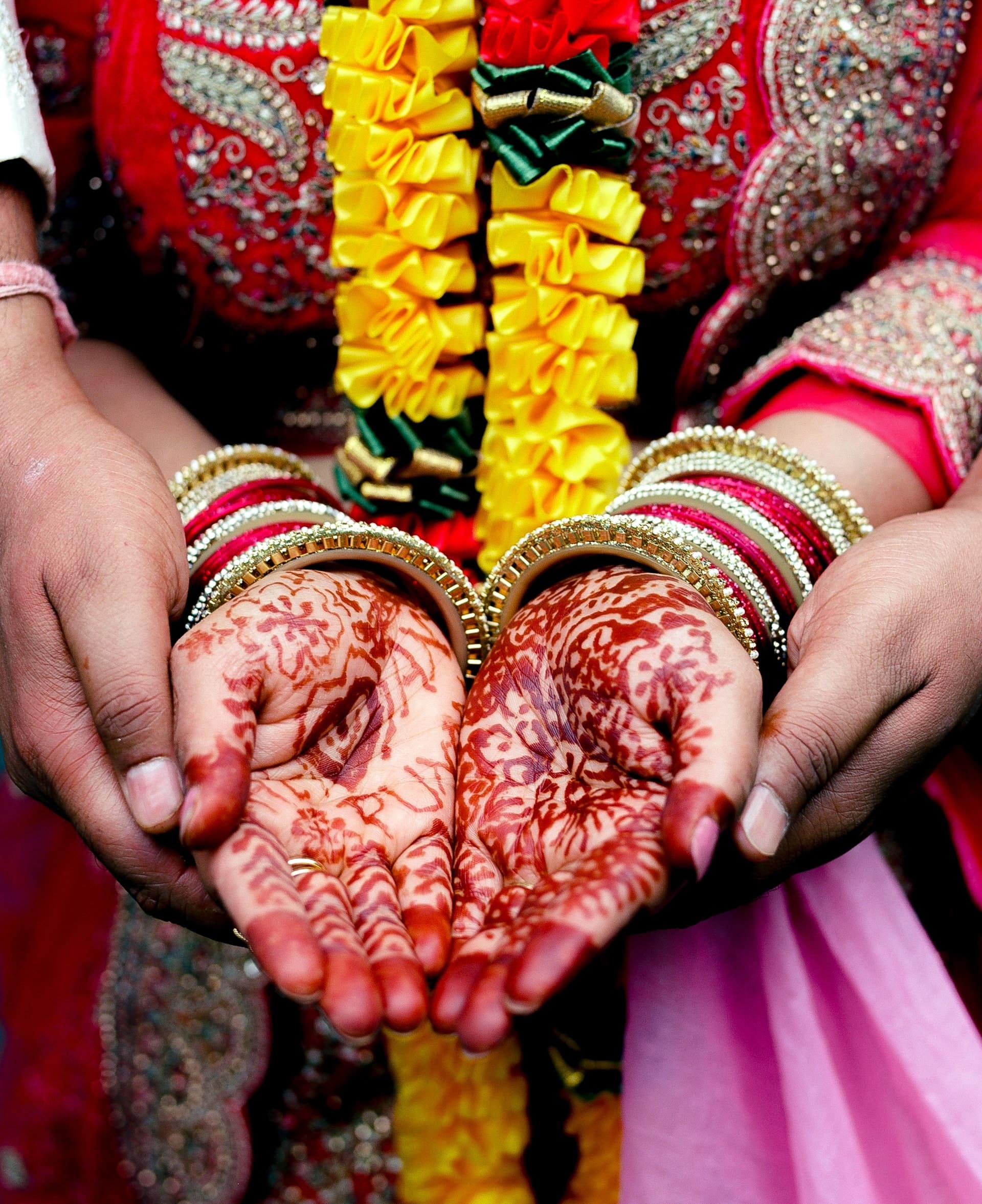 Bride's hands decorated with henna, holding flower garlands, at an Indian wedding
