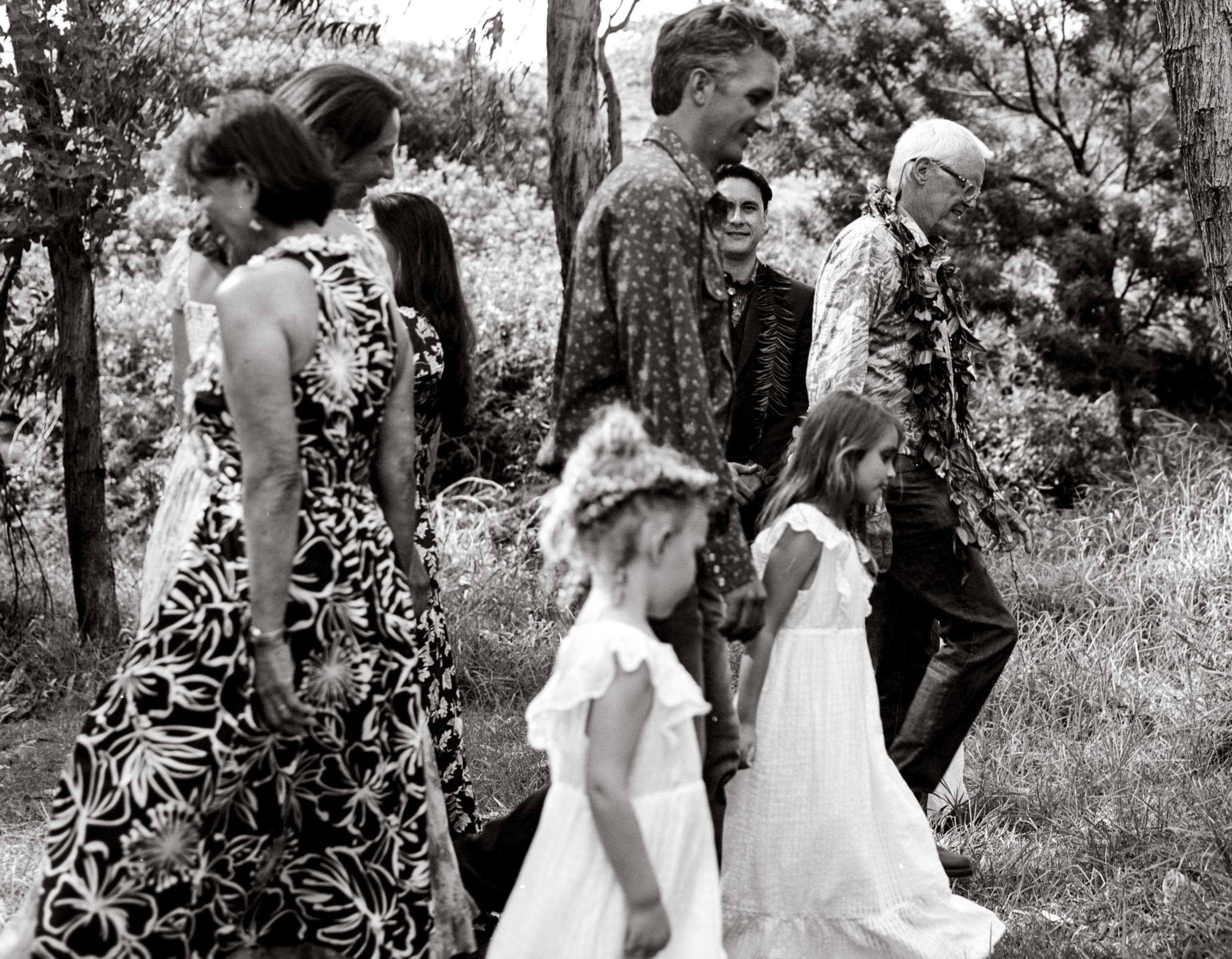 Black and white candid of wedding guests and flower girls walking through trees