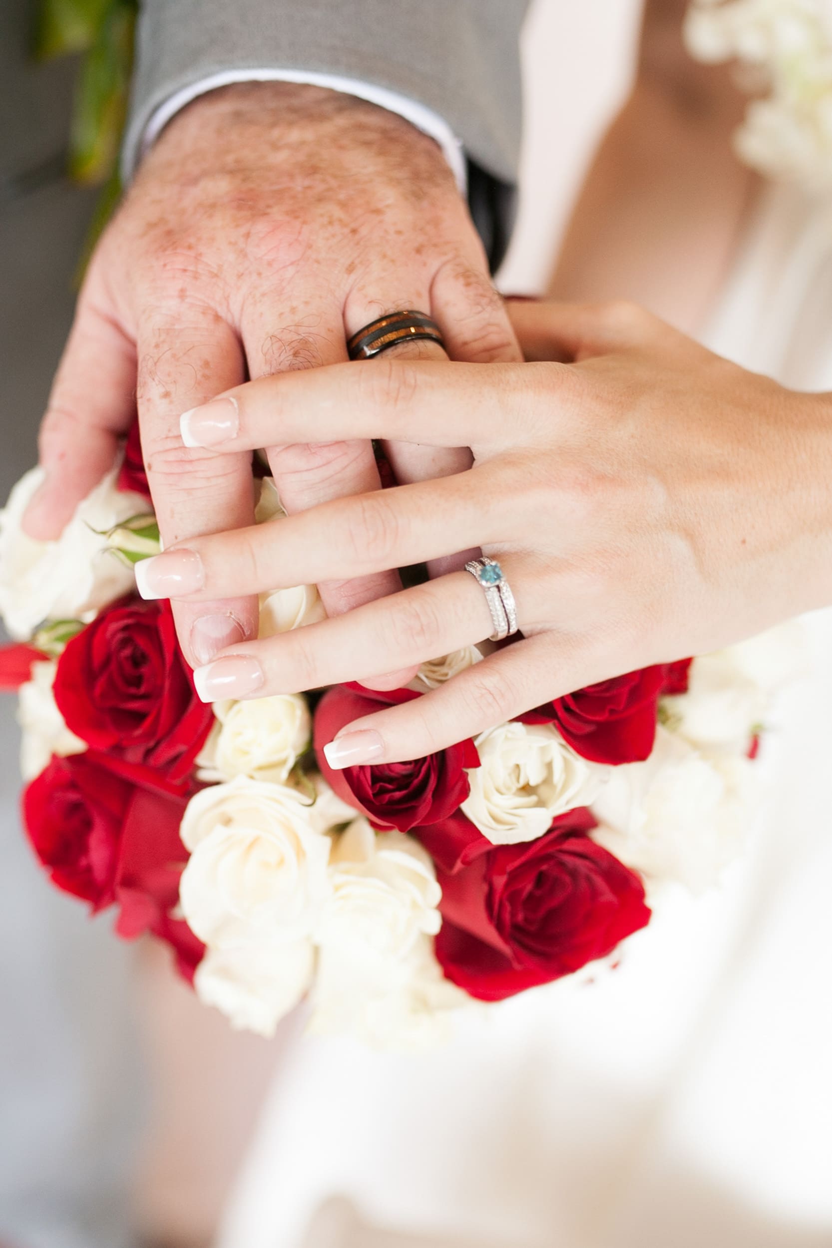 Hand with a wedding ring resting on a bouquet of red and white roses