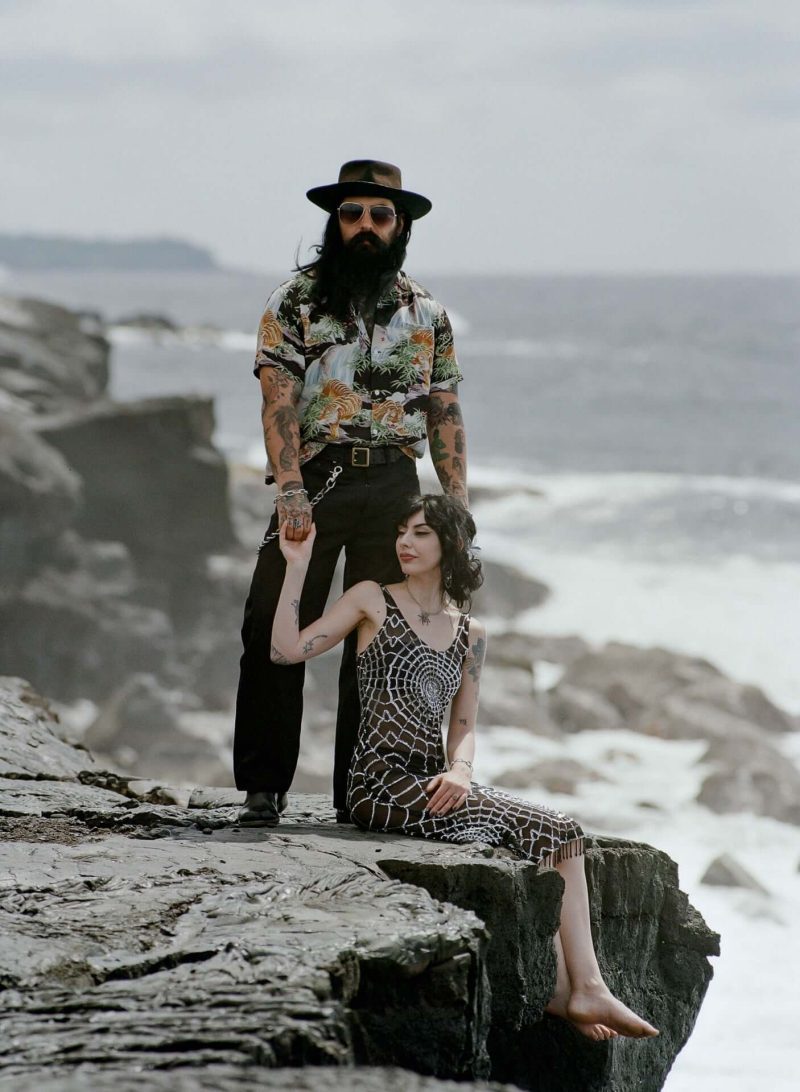 Couple posing on a rocky ocean ledge with waves behind them