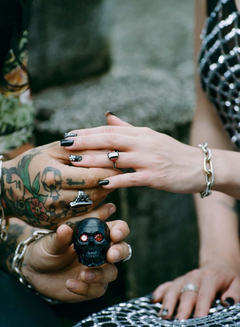 Close-up of tattooed hands with rings holding a small skull
