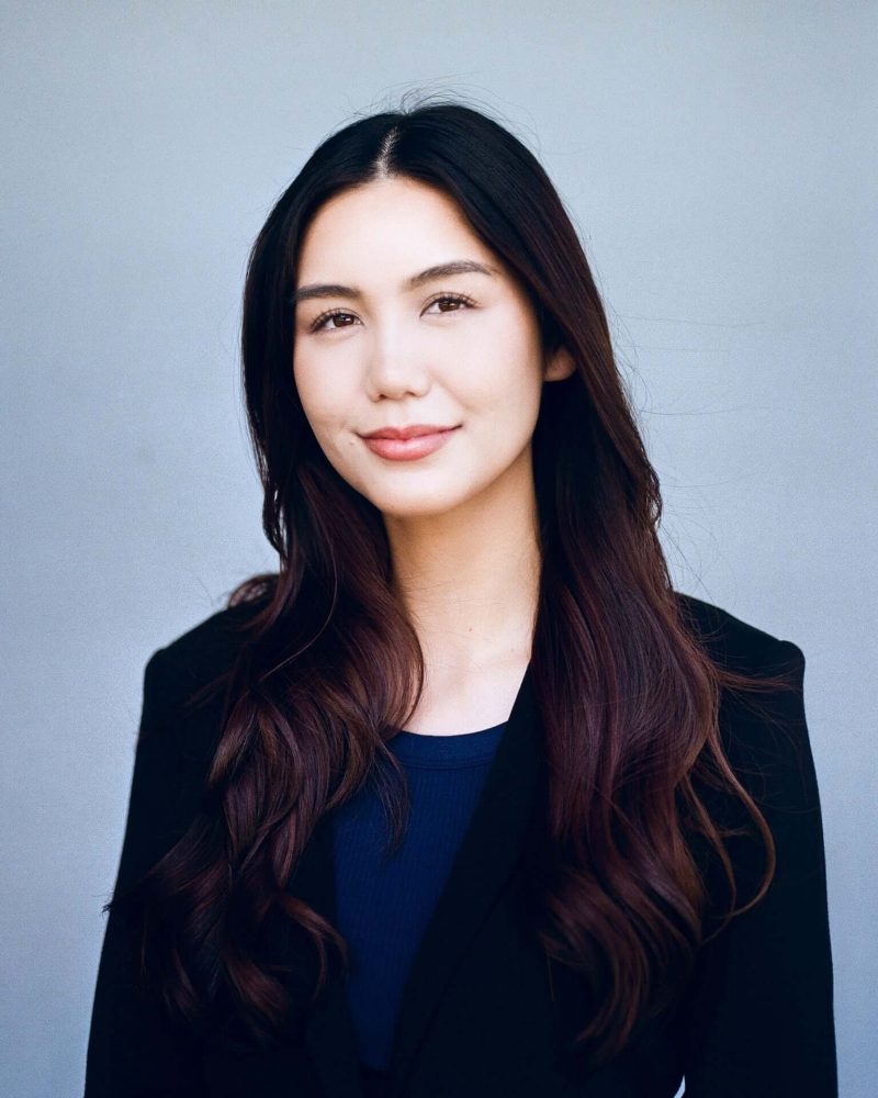 Headshot of a woman in a black blazer against a blue-gray backdrop