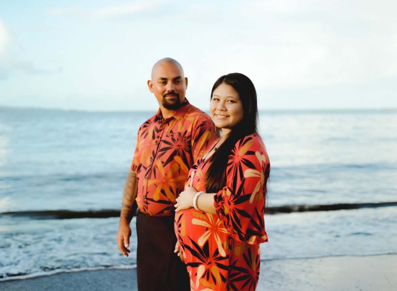 Expecting couple in matching aloha prints on the beach