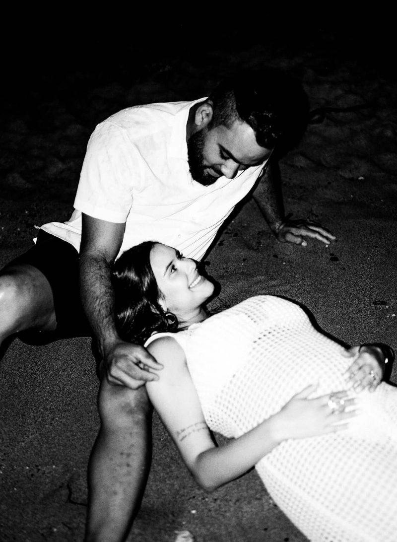 Black and white photo of a man leaning over his pregnant partner lying on the ground