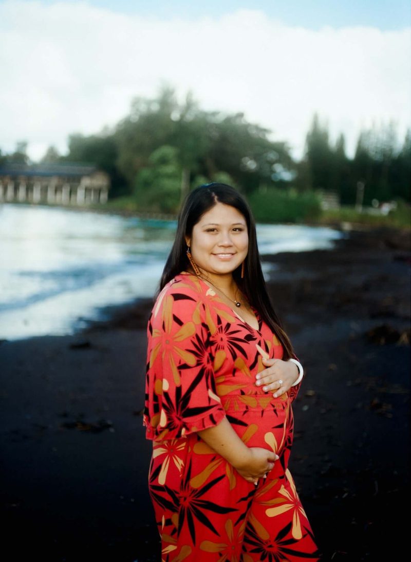 Pregnant woman in a red floral dress on a black sand beach