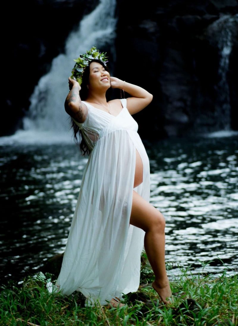 Expectant mother in a white gown in front of a waterfall