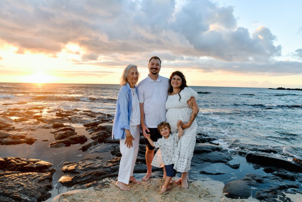 Three-generation family on lava rock at sunset under a dramatic sky, flash-lit family portrait in Kona Hawaii