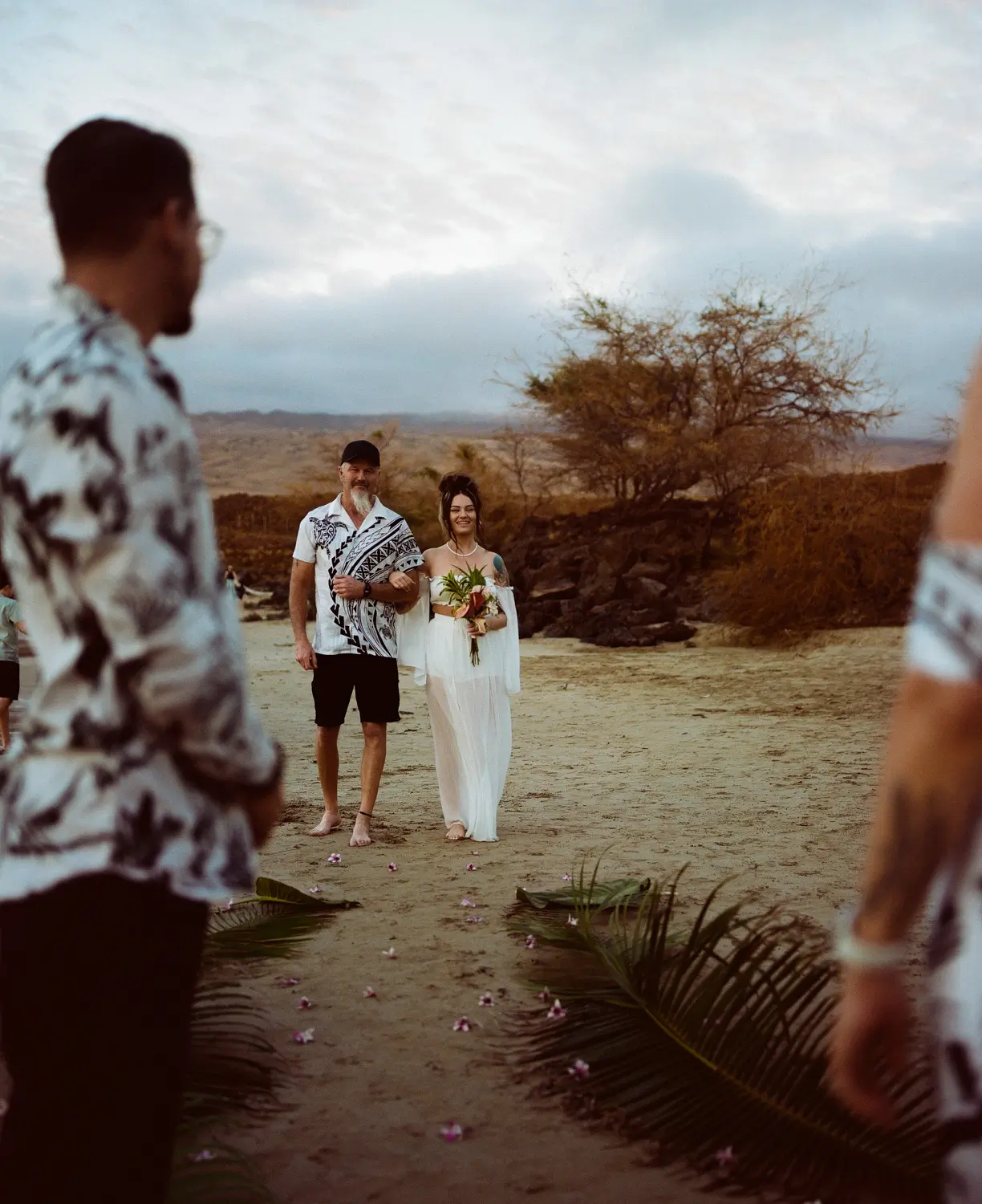 Bride and groom walking down a sandy aisle toward guests
